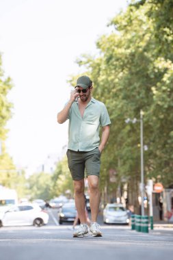 Genç adam güneşli bir günün tadını çıkarıyor. Sokakta yürüyor ve telefonla konuşuyor.