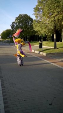 Sokak sanatçısı parkta renkli kurdelelerle hokkabazlık yapıyor, yavaş çekimde dikey bir videoda.