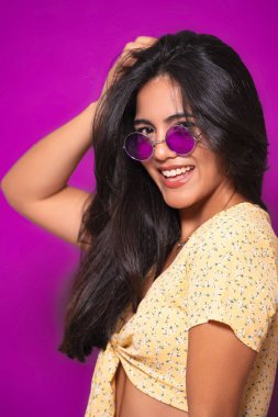 Uzun saçlı, mor güneş gözlüklü, ve sarı çiçekli bluzlu, neşeli bir poz veren bir kadın.. 