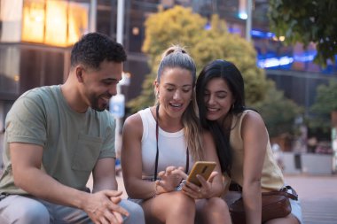 Üç arkadaş gülerek ve akıllı bir telefon kullanarak yazın arkadaşlığın ve teknolojinin neşesini sergiliyorlar.