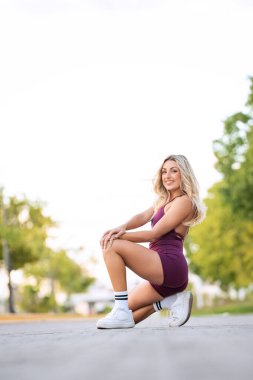 Sportif kadın antrenmanına ara veriyor. Parktaki kaldırımda diz çöküyor.