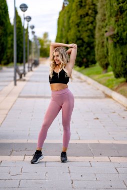 Sarışın sporcu kadın şehir parkında antrenman yapmadan önce kollarını açıyor.