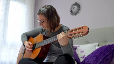 Kadın yatak odasında akustik gitar çalmayı seviyor. Müzik ve tutkuyla dolu rahatlatıcı bir atmosfer yaratıyor.