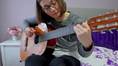 Müzisyen akustik gitarıyla bir melodi çalıyor, ellerini yavaş çekimde detaylıca gösteriyor.