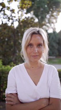 Sarışın kadın ağır çekimde neşeyle gülümsüyor güneşli bir açık hava parkında mutluluk ve güzellik sergiliyor.