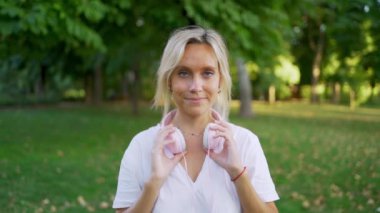 Genç bir kadın parkta kulaklık takıyor, müzikten hoşlanıyor ve güneşli bir yaz gününün huzurunu kucaklıyor.