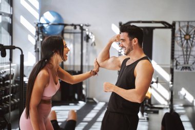 Spor salonunda birlikte egzersiz yaptıktan sonra vücut geliştirme uzmanı kadın partnere kol kaslarını gösteriyor. Spor konsepti.