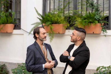 Binanın dışında sohbet eden iki iş adamı, biri dizüstü bilgisayar tutuyor, işle ilgili bir tartışma öneriyor.