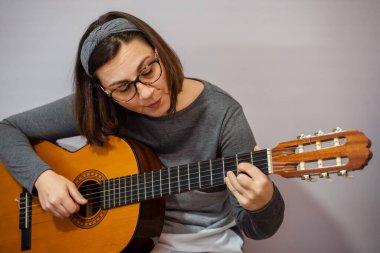 Klasik gitar çalan ve evde şarkı söyleyen, müziğe dalmış, yeteneğini ve hobisini sergileyen bir kadın.