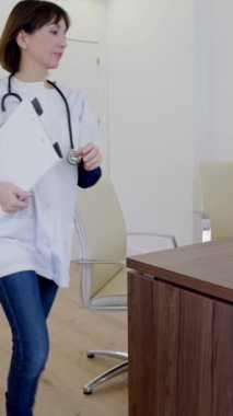 Profesyonel kadın doktor masasına gider ve bilgisayar ve tıbbi kayıtları üzerinde çalışmaya başlar.