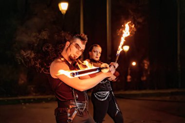 Two fire dancers captivating the audience with their skillful performances, twirling burning staffs amidst the vibrant energy of a night show clipart