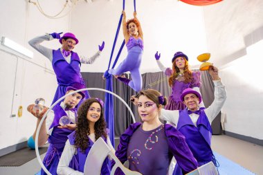 Mor kostümlü bir grup sirk göstericisi yeteneklerini sergileyerek prova alanlarında birlikte poz veriyorlar.