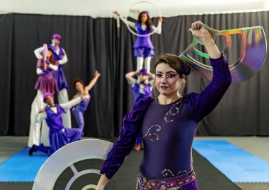 Sirk göstericileri prova sırasında çeşitli aksesuarlar tutuyorlar, yeteneklerini ve koordinasyonlarını sergiliyorlar.