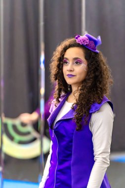 Cosplayer canlı mor bir kostüm ve karmaşık bir makyaj giyer, yumuşak bulanık bir arka plana karşı poz verir.