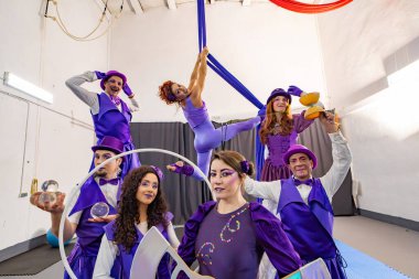 Bir eğitim tesisinde birlikte poz veren bir grup sirk göstericisi, hokkabazlık, denge ve hava akrobasisi yapıyor.