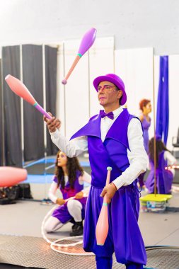 Bir sirk okulu eğitimi sırasında arka planda diğer sanatçılarla kulüplerle hokkabazlık yapan erkek sanatçı.