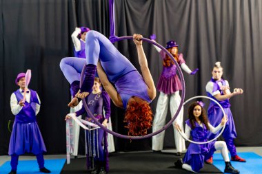 Sirk gösterisi sırasında arka planda poz veren ve hokkabazlık yapan kızıl saçlı akrobat.