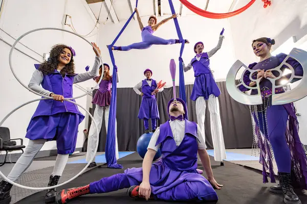 Canlı mor kostümlü sirk sanatçıları hulahop, hokkabazlık ve hava akrobasisi gibi yeteneklerini sergiliyorlar.