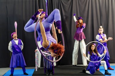 Mor kostümlü bir grup sirk sanatçısı çemberler ve diğer sirk elemanlarıyla gösteri yapıyorlar.