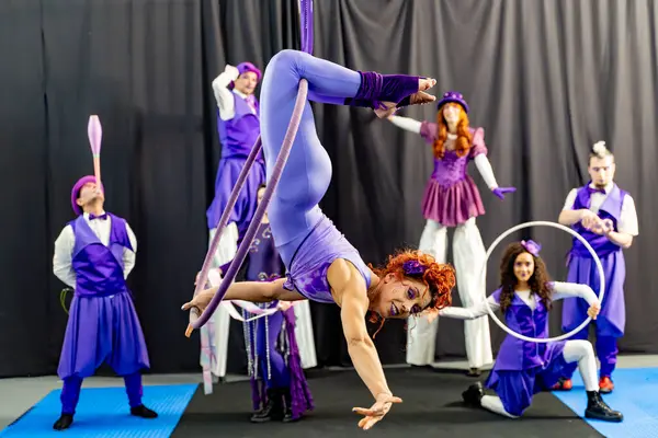 Kızıl saçlı akrobat, sirk sanatçılarıyla çevrili bir hava çemberinde gösteri yapıyor. Takım çalışmasını ve sanatını ön plana çıkarıyor.