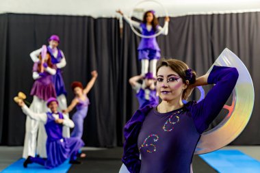 Sirk sanatçıları canlı mor giysiler içinde, sahne malzemeleriyle yeteneklerini sergiliyorlar ve büyüleyici bir sanat sahnesi yaratıyorlar.