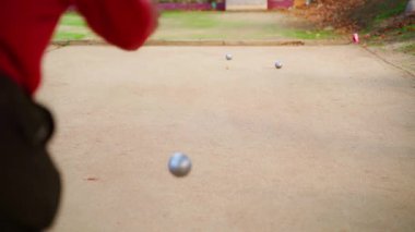 Petanque oyuncusu, rekabetçi açık hava aktiviteleri sırasında hassas bir şekilde heavy metal bulvarı fırlatıyor. Kumlu mahkeme geçmişine karşı konsantre bir yetenek sergiliyor.