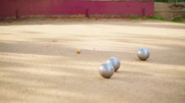 Metalik bocce topları kumlu sahada zarifçe yuvarlanıyor, yavaş çekimde açık hava oyunu sırasında hassas küçük krikoyu hedef alıyor.