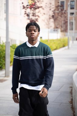 Kampüs kaldırımında yürüyüp temiz havanın ve akademik atmosferin tadını çıkaran kendinden emin genç bir üniversite öğrencisi.