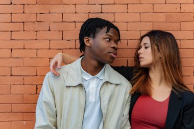 Birbirlerini kucaklayan ve birbirlerine dik dik bakan çok ırklı genç bir çift. Birbirleriyle olan bağlarını güçlendiren zarif tuğla bir duvarla çevrili.