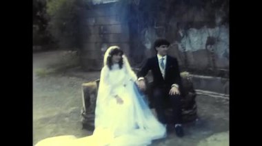 palermo,italy december 1980: happy bride and groom sitting holding hands in the park in the 80s