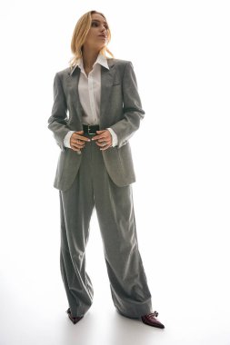 Genç bir kadın modern tarzını sergiliyor, büyük gri bir takım giymiş, zarafet saçıyor..