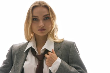 Özel dikim ceketli ve kravatlı şık genç bir kadın parlak bir alanda rahatça poz verir..