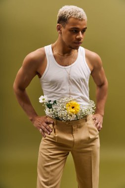 Şık bir genç adam, atölyede renkli çiçeklerle süslenmiş bir atlet içinde güven içinde poz verir..