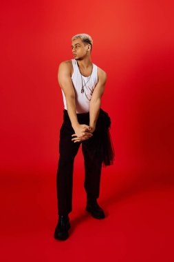 Şık bir genç adam kendine güvenen bir şekilde kırmızı bir stüdyoda poz veriyor, eşsiz tarzını sergiliyor..