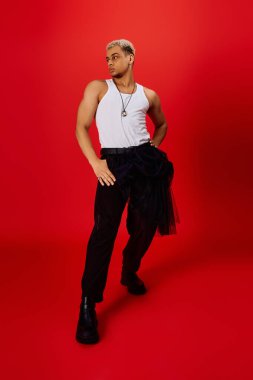 Afro-Amerikalı şık bir genç adam kırmızı bir stüdyoda moda modelliği yapıyor, kendine güveni yüksek..