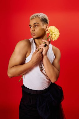 Saçları boyalı genç adam elinde çiçekle şık bir bluzla rahatça poz veriyor..