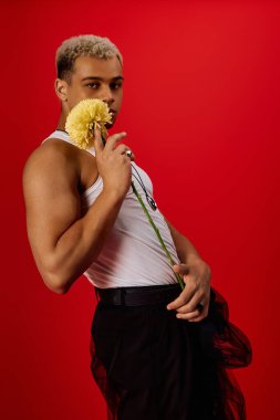 Tarz sahibi genç bir siyah adam kırmızı bir arka plana karşı elinde çiçekle poz verir..