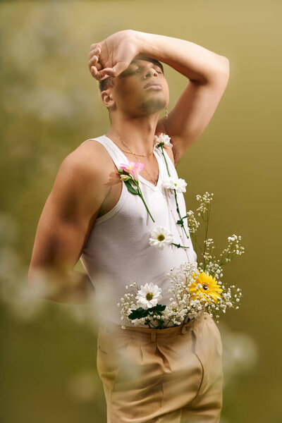 A young man poses confidently in a stylish tank top with fresh flowers in a creative studio setting.