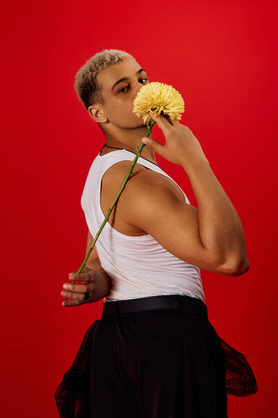 Young man with dyed hair poses confidently with a flower in a trendy studio.