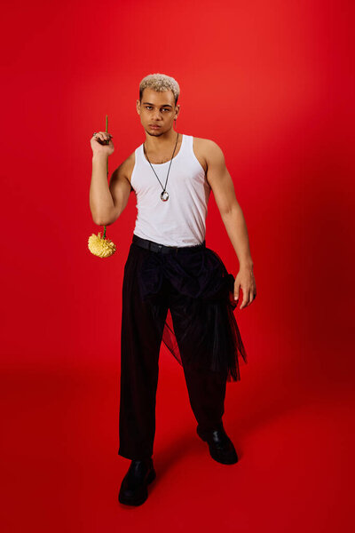 Стильный молодой афроамериканец уверенно позирует в майке и черных штанах.