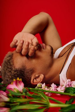 Genç ve modaya uygun bir adam, çiçeklerle çevrili renkli bir zeminde sanatsal poz verir..