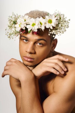 Tişörtsüz genç bir adam, parlak bir stüdyoda çiçek tacıyla güzelliğini ve tarzını sergiliyor..
