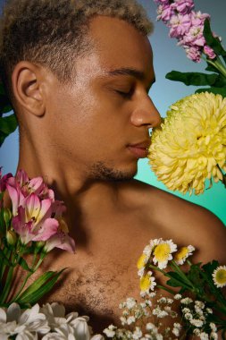 Saçları boyalı genç bir adam etrafındaki renkli çiçeklerle nazikçe etkileşime girer..