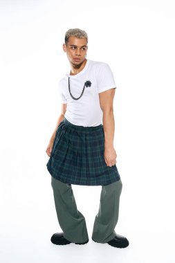 Genç adam modern bir kıyafetle poz veriyor, canlı bir stüdyo ortamında cesur tarzları harmanlıyor..