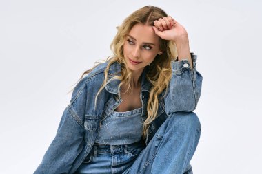 Güzel bir sarışın manken şık bir kot giysi, temiz bir arkaplana karşı özgüven yayıyor..