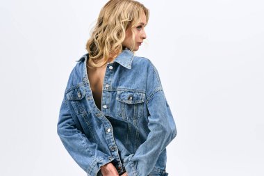 Kot ceketli sarışın kadın minimalist bir arkaplanda zarif bir poz veriyor..