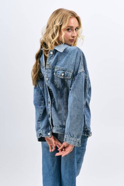 Sarışın, güzel bir genç kadın, kendine güvenen, modaya uygun kot giyimli, büyüleyici bir şekilde poz veriyor..