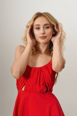 Sarışın kadın zarif tarzını sergilerken kendine güvenen kırmızı bir elbise giyiyor.