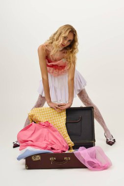 Şık bir genç kadın eski bir bavulun yanında şık kıyafetler sergiliyor, canlı bir hava yaratıyor..