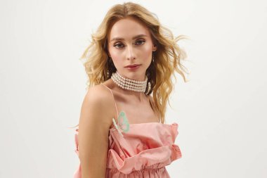 Genç sarışın bir kadın kelebek süslemeli pembe bir elbise mankenliği yapıyor..